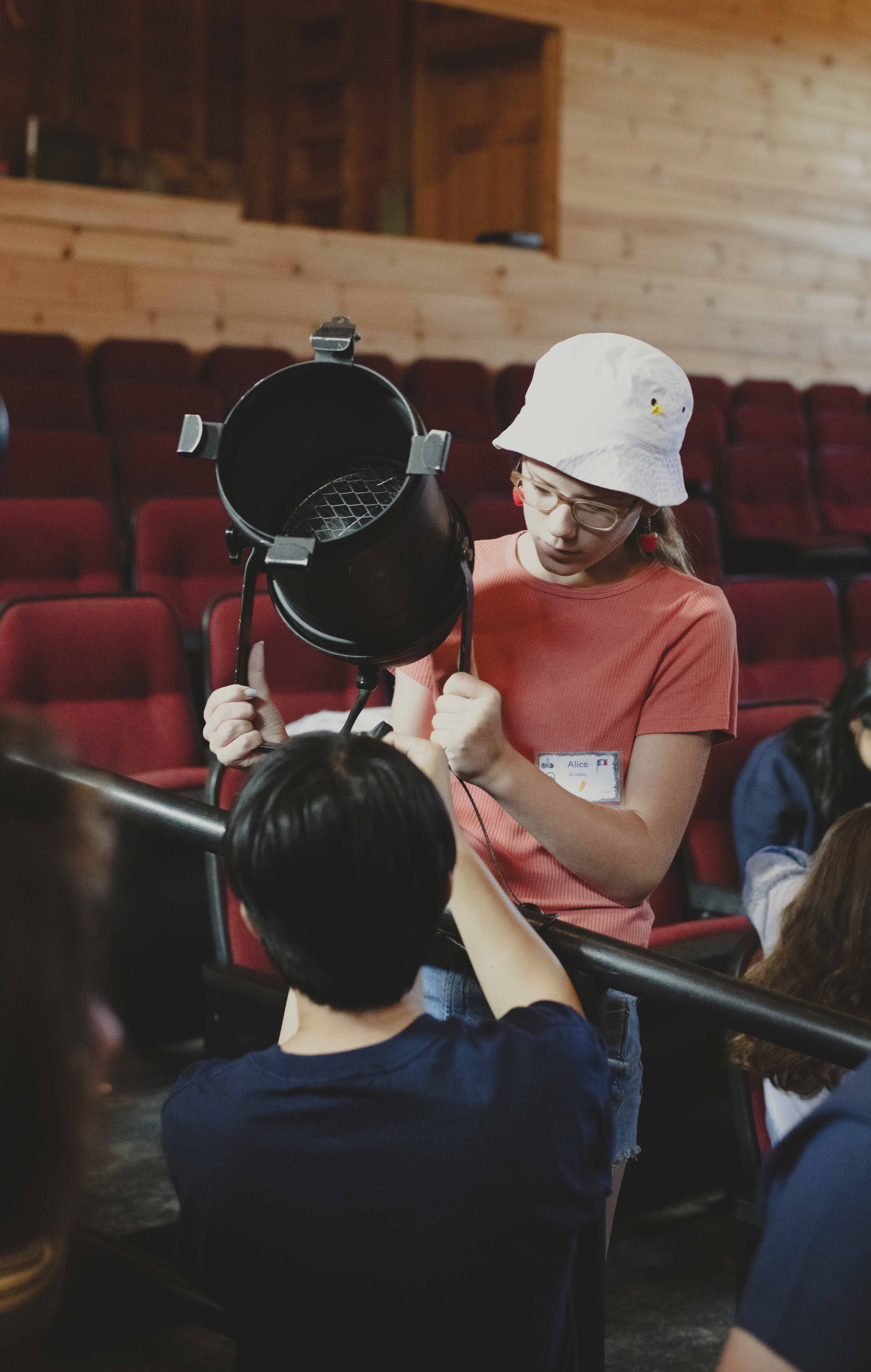 A camper hangs and focuses a light fixture in the theater.